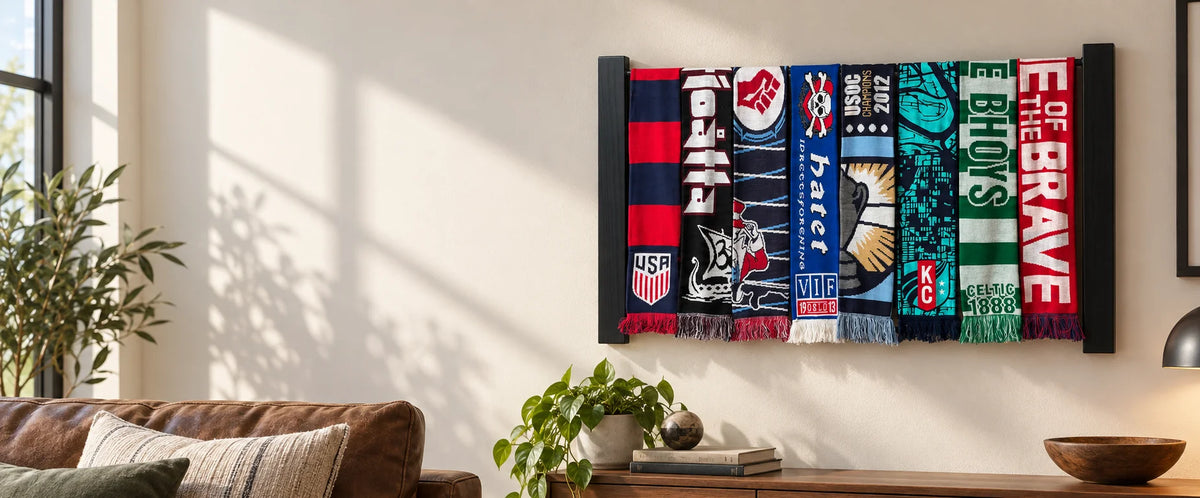Two-row rack of soccer scarves on a cream living room wall beside a leather sofa